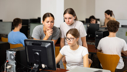 Fototapeta premium Two smart female teenagers in casual clothes, giving a clue to the co-learner while using pc in computer classrooms