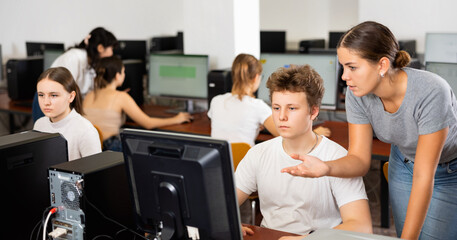 Fototapeta premium Young woman teacher helping concentrated teen male student with his work in college computer class
