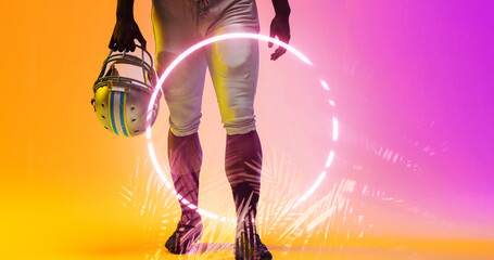 Low section of american football player holding helmet walking by illuminated circle and plants
