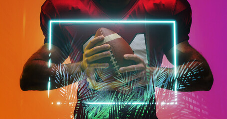 Midsection of american football player with ball standing by illuminated rectangle and plants