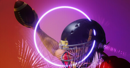 Close-up of american football player wearing helmet raising hand with ball by circle and plants