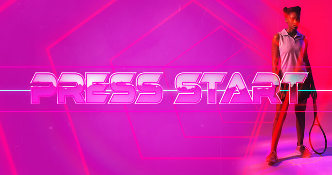 Biracial female athlete with racket standing by press start text and lines on pink background