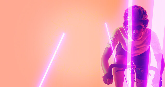 Biracial female athlete riding bike by illuminated lines over peach background, copy space