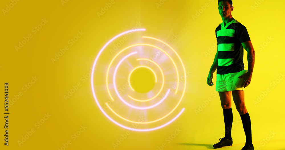 Poster full length of caucasian rugby player with ball standing by illuminated circular pattern, copy space