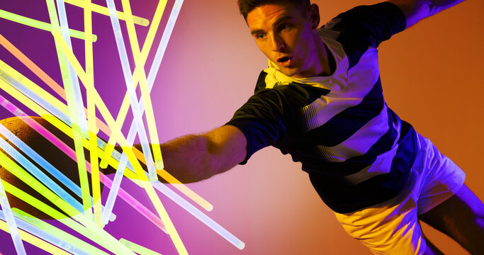 Caucasian rugby player jumping and catching ball by colorful glowing lines on colored background