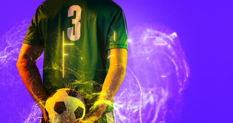 Rear view of soccer player holding ball with abstract neon in blue background, copy space