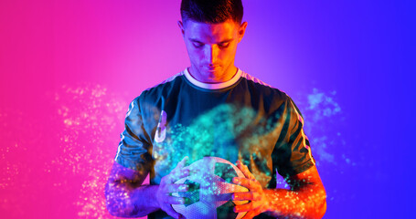 Caucasian young soccer player holding ball with abstract design over blue and pink background