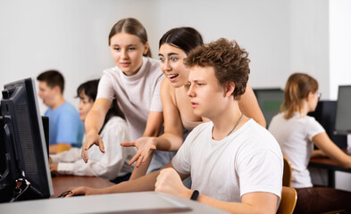 Positive young boy and girls using personal computer together. Cheerful teenagers in computer class.