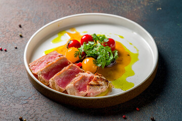 grilled tuna fillet with vegetables on plate on dark stone table