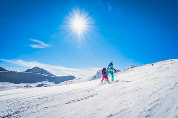 Mother and daughter preparing to descend on a ski slope. Sunny day on ski winter holidays in Andorra, El Tarter, Pyrenees Mountains - obrazy, fototapety, plakaty