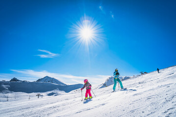 Mother teaching daughter how to ski, skiing down on a ski slope. Sunny day on ski winter holidays...