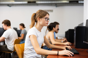Smart teenager girl in glasses using computer during computer sciene lesson in school.