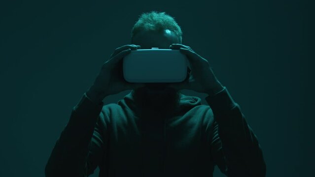 Astonished guy holding augmented reality tool. Portrait of a man wearing VR goggles in dark neon-colored room. High quality 4k footage