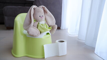 Soft toy bunny sitting on a baby green plastic potty and toilet paper