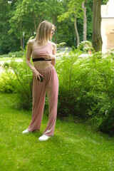 Girl in the pink topic and black summer sunglasses walking in the green park