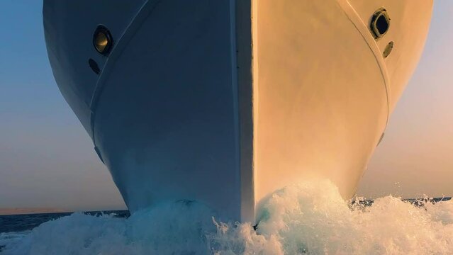 Sailboat prow and white foam water splashes close up front view. Yachting, ocean sailing, sunrise sun light on vessel forepart, boat bow closeup