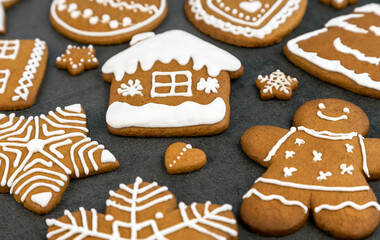Christmas gingerbread cookies with icing on a gray background in the shape of a house and a gingerbread man, a Christmas tree and balls, stars and snowflakes and hearts. Close up.