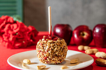 peanut covered red candy apple on white plate with peanuts and apples in background