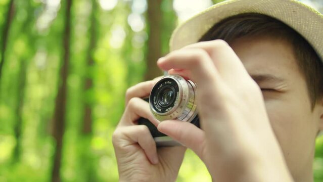 travel teenager boy takes pictures in the forest with an old camera in summer, close up