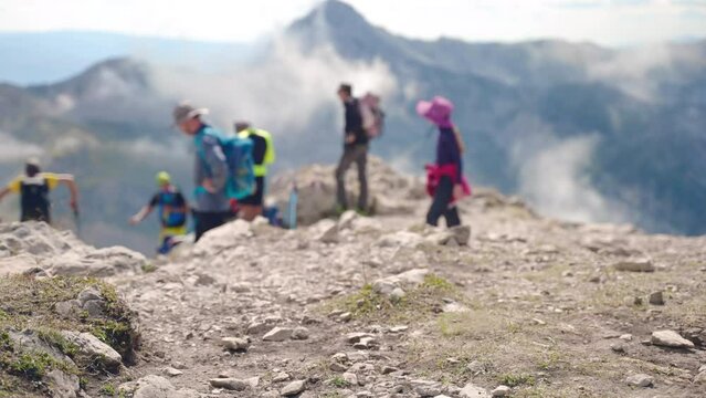 Amazing mountains peak with sharp ranges and raising fog, blurred people in sport clothes and with backpacks relaxing on the ground after long hiking, adventures in the mountains, sport and relax