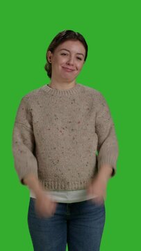 Vertical video: Front view of cheerful model doing thumbs up symbol in studio, expressing approval and like gesture over greenscreen. Female person acting positive and happy, showing agreement and