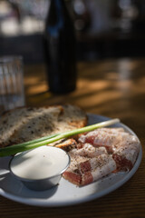 Close up view slices of smoked bacon meat with rye whole grain black bread, green onion and sour cream on the table.