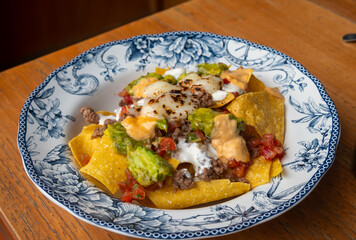 Corn chips nachos with fried minced meat and guacamole on wooden background.