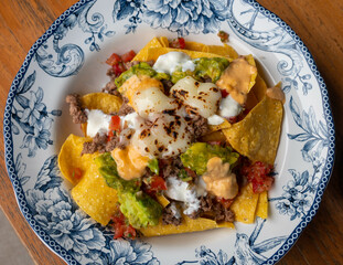 Corn chips nachos with fried minced meat and guacamole on wooden background.
