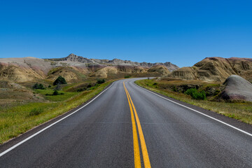 Highway curves through landscape of grassland and colorful peaks in Badlands National Park