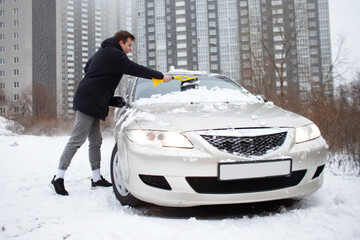 guy cleans the snow with a brush from the car, a man takes care of the car in winter