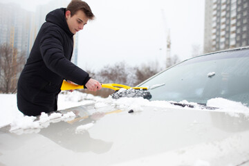 guy cleans the snow with a brush from the car, a man takes care of the car in winter