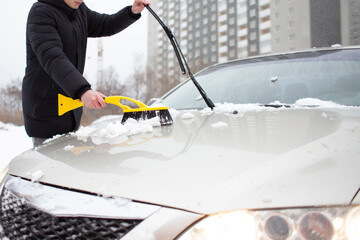 guy cleans the snow with a brush from the car, a man takes care of the car in winter