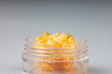 glass jar with golden cannabis wax, pieces of hardened resin of marijuana extract on an gray...