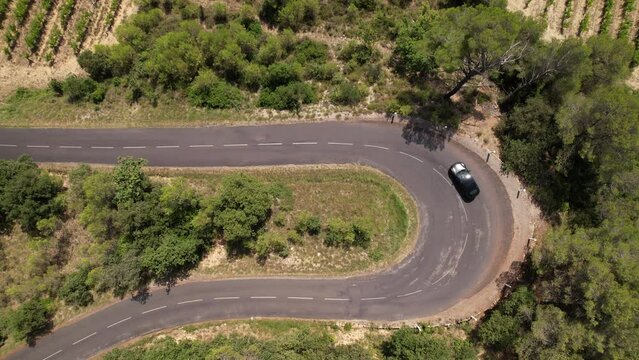 Aerial top shot over an winding road with electric car passing South of France sunny 