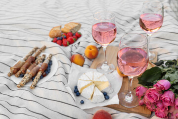 Glasses of delicious rose wine, flowers and food on white picnic blanket