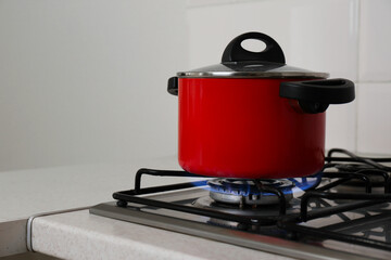 Red pot on stylish kitchen stove with burning gas, space for text