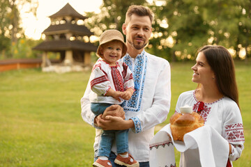 Happy cute family in embroidered Ukrainian shirts with korovai bread on sunny day. Space for text