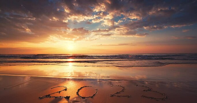 Happy New Year 2023 text in sand, ocean sunrise on the beach shore. Golsen sea sunset.