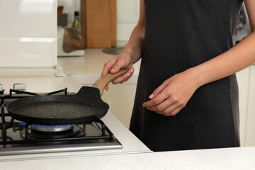 Woman putting frying pan on stove with burning gas in kitchen, closeup