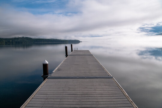 Perspective view of boat dock over tranquil lake reflecting blue sky, clouds, and fog at Lake McDonald, Glacier National Park, Montana