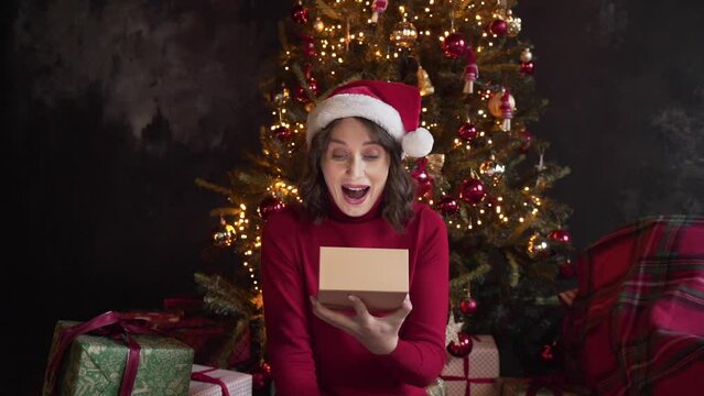 A young beautiful woman is opening a gift box, light shines on her face. 
