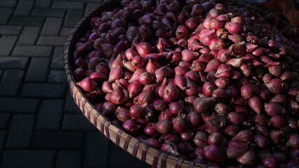 Piles of shallots on a bamboo basket exposed to the morning sun at a traditional market. Focus is selected
