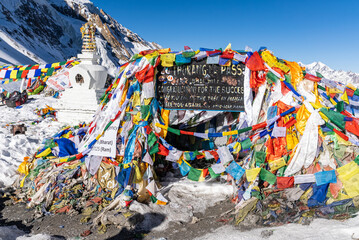 Signboard and prayer flags on the Thorang La pass. Scene in the Annapurna Conservation Area, Nepal.