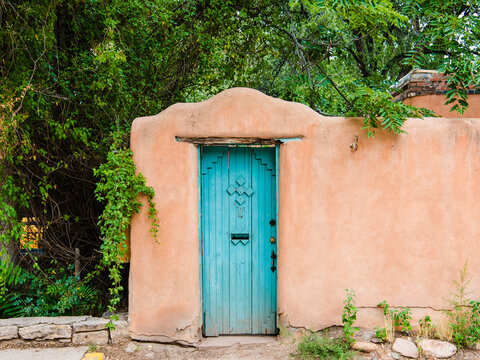 Rustic turquoise colored wood door set in an old adobe wall in Santa Fe, New Mexico