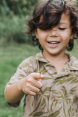 long hair little boy holding a frog in nature