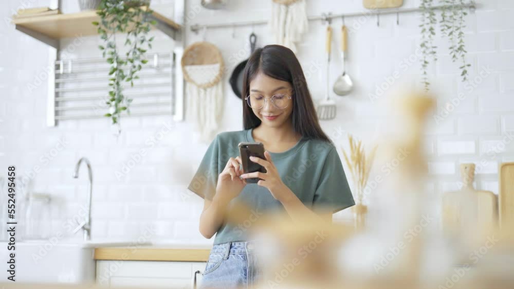 Poster happy young asian woman wearing glasses and relaxing at home. asia female standing at counter kitche