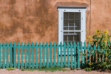 Obraz premium Sunflowers and turquoise color wood fence set in front of a window and old adobe wall along Canyon Road in Santa Fe, New Mexico