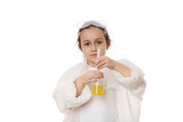 Smart primary school student, little girl in lab coat, using laboratory glass stick, mixes yellow chemical solution in beaker, shows the ongoing chemical reaction, looking at camera, white background