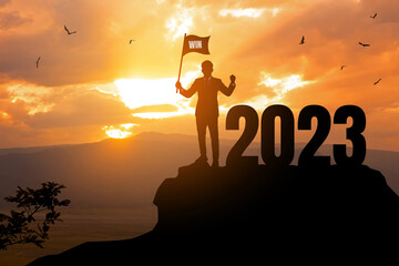 2023 New year Success concept.silhouette of businessman holding winner flag with 2022 on the...