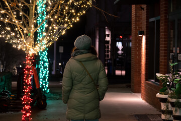 Obraz premium woman walking alone next to tree decorated with Christmas lights